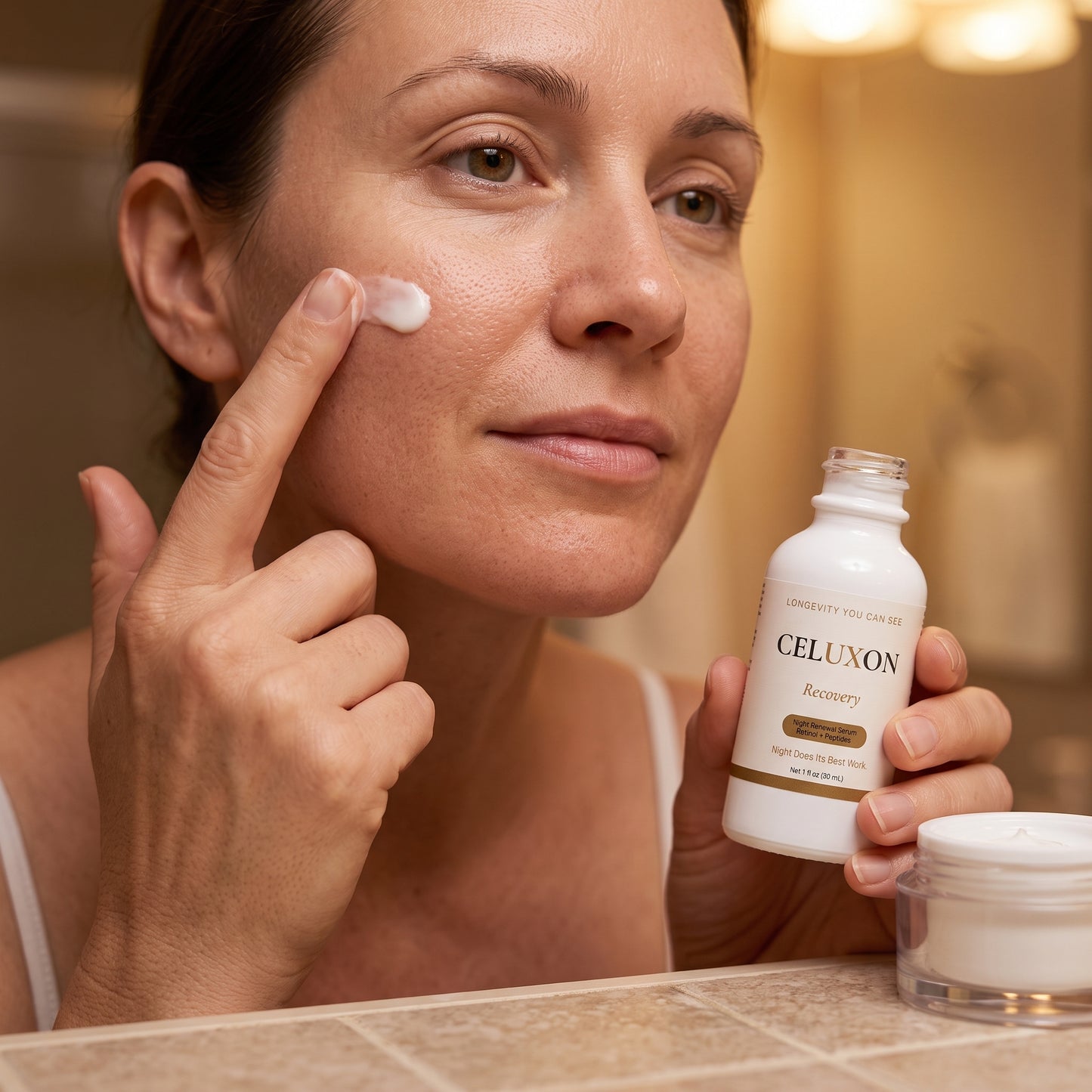 A woman in a bathroom applies a white cream to her cheek while holding a bottle of CELUXON Recovery facial cleanser and a small jar on the counter.